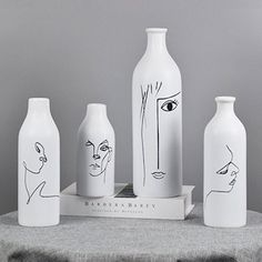 five white vases sitting on top of a table with faces drawn on the bottles