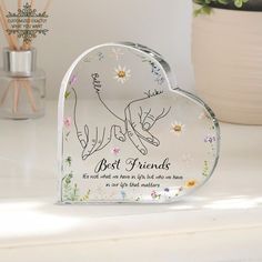 a glass heart shaped object with the words best friends on it and flowers in the background