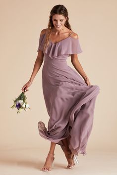 a woman in a purple dress holding a flower and smiling at the camera while walking