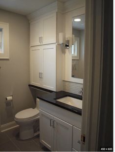 a white toilet sitting next to a sink in a bathroom under a mirror and cabinet