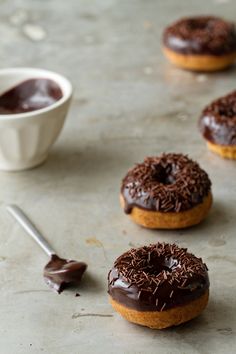 chocolate covered doughnuts with sprinkles and a spoon next to them