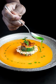 a person is holding a spoon over a plate with food on it and garnishes