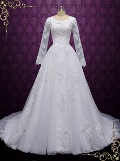 a white wedding dress with long sleeves and lace on the bouncy skirt is displayed in front of a purple background