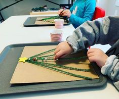 two children are making christmas trees out of beads and paper plates on a tray at a table