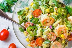 a salad with shrimp, tomatoes, corn and avocado in a glass bowl