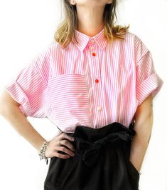 a woman with her hands on her hips wearing a pink and white striped shirt, black skirt and silver bracelets