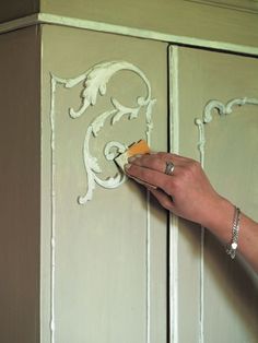 a woman is painting the side of a cabinet with white paint and an ornate design on it