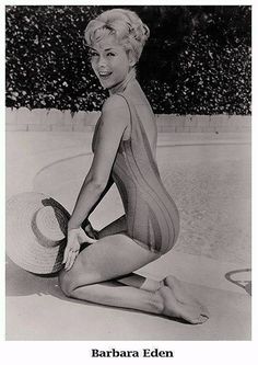 an old photo of a woman in a bathing suit and hat sitting on the ground