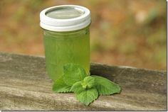 a glass jar filled with green liquid sitting on top of a wooden table next to a sprig of mint