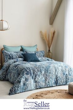 a bed with blue comforters and pillows in a room next to a window,