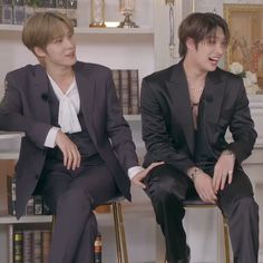 two young men sitting next to each other in front of bookshelves and shelves