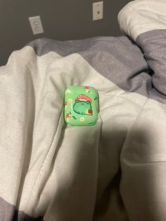 a close up of a pillow on a bed with a green frog applique