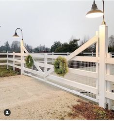 a white fence with wreaths on it and two lights hanging from the top one