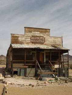 an old run down building sitting in the middle of nowhere on a dirt lot with stairs leading up to it