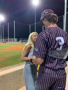 a man and woman in baseball uniforms standing next to each other on a field at night