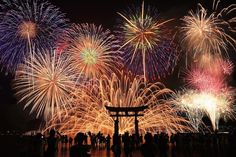 fireworks are lit up in the night sky over a body of water with people standing around it