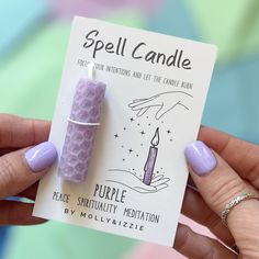 a hand holding a purple candle on top of a piece of paper with the words spell candle