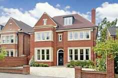 a large red brick house with many windows and bushes on the side of the road