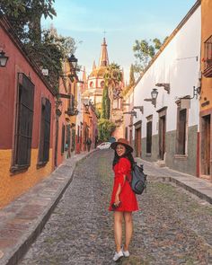 a woman in a red dress and hat walking down a cobblestone alleyway