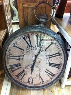 an old clock with roman numerals is on the floor next to a table