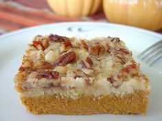 a white plate topped with a piece of cake covered in frosting and pecans