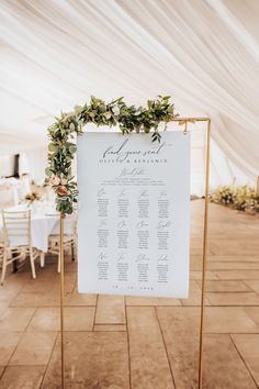 a sign that is sitting on top of a table with flowers and greenery around it