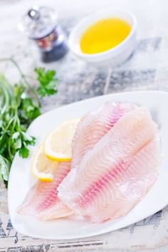 two raw fish fillets on a plate with lemons and parsley next to it