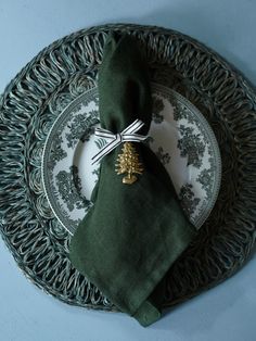 a place setting with a green napkin and pine tree decoration on the side, sitting on a wicker plate