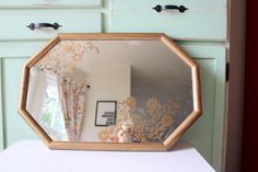 a mirror sitting on top of a white table next to a dresser with drawers and curtains