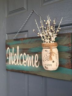 a mason jar hanging from a door with the word welcome painted on it and flowers