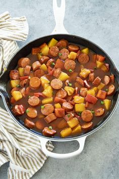 a skillet filled with sausage and potatoes on top of a table next to a striped towel