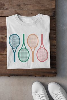 three tennis rackets on a white t - shirt next to two pairs of shoes