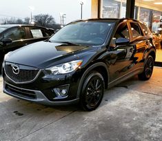 a black mazda car parked in front of a building with two other cars behind it