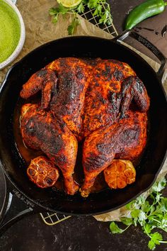 a cooked chicken in a skillet with spices and seasoning on the table next to it