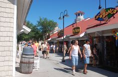 people are walking down the sidewalk in front of shops and stores on a sunny day