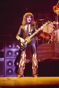 a man with long hair and leather pants on stage holding a guitar in front of him