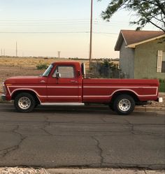 a red pick up truck parked on the side of the road in front of a house