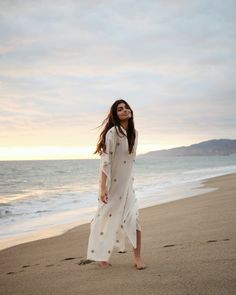 A natural white caftan made in handspun jamdani cotton fabric. It is accented with delicate handwoven motifs all over, V-shaped neckline, wide sleeves and side slits. This breathable caftan is mindfully crafted from sustainable materials and can be worn as a beach cover-up or worn out with slip. - Length: 51” - Fabric: Handwoven cotton - Color: Off-white White Chikankari Embroidery Kaftan For Vacation, White Long Kurta For Beach, Long White Kurta For Vacation, White Chikankari Embroidery Kaftan For Beach, White Caftan, Beach Covers, Wide Sleeves, Sustainable Materials, V Shape