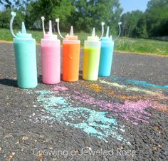 four different colored bottles are lined up on the pavement with chalk crayons all over them