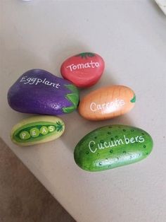 four painted rocks that say cucumbers, tomato, eggplant and carrots