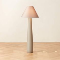 a white lamp sitting on top of a hard wood floor next to a beige wall