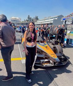 a woman standing next to a race car in a parking lot with other people around