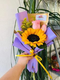 a person holding a bouquet of flowers in front of a potted plant with pink roses and yellow sunflowers