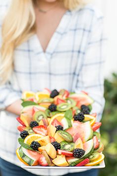 a woman holding a platter of fruit salad