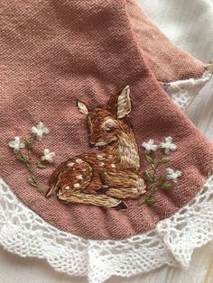 an embroidered deer sitting on top of a pink piece of cloth with white lace around it