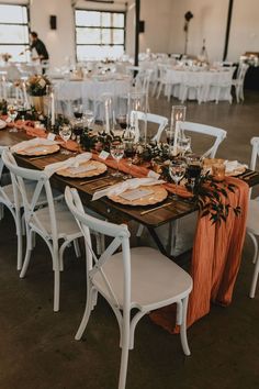 a long table set up with white chairs and orange napkins on top of it