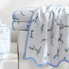 two white towels with blue flowers on them are sitting next to each other and one is folded up