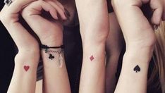 three girls with matching tattoos on their arms holding hands up to each other and looking at the camera