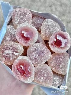 a person holding a box filled with sugar covered donuts and jelly filling toppings