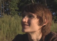 a woman with glasses is standing in front of some tall grass and trees, looking off into the distance